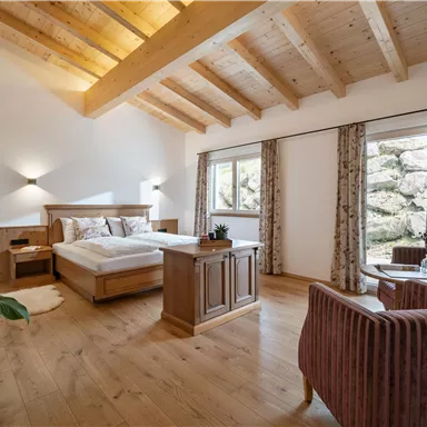 Ein helles Schlafzimmer mit Holzdecke und einem großen Bett. Zwei bequeme Sessel und Fenster mit Blick nach draußen ergänzen den Raum.