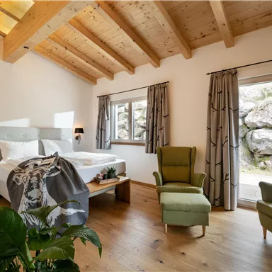 Ein modernes Schlafzimmer mit Holzbalkendecke und großen Fenstern. Es gibt ein bequemes Bett und einen gemütlichen Sessel.