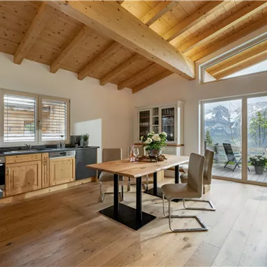 Ein modernes Esszimmer mit Holzoberflächen und großen Fenstern. Im Hintergrund sieht man eine schöne Berglandschaft.