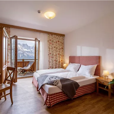 Ein gemütliches Hotelzimmer mit einem großen Doppelbett und einem Balkon. Der Raum ist modern eingerichtet und bietet einen Blick auf die Berge.