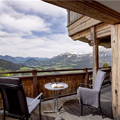 Ein gemütlicher Balkon mit Blick auf die majestätischen Berge und die grüne Landschaft. Zwei Stühle und ein Tisch laden zum Entspannen ein.