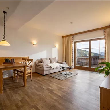 Ein gemütliches Wohnzimmer mit einem Sofa, einem Esstisch und Stühlen. Große Fenster bieten Aussicht und natürliches Licht.