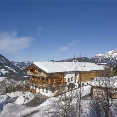 Ein malerisches Chalet in verschneiter Winterlandschaft. Im Hintergrund erstrecken sich schneebedeckte Berge unter einem klaren blauen Himmel.