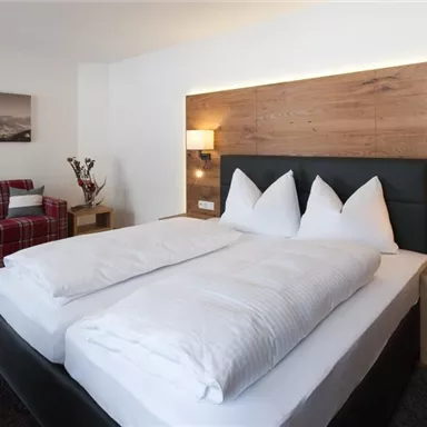 A modern hotel room with a large bed and elegant wood paneling. A cozy couch and soft lighting create an inviting atmosphere.