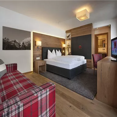 A modern hotel room with a large bed and a cozy couch. The wood and fabric elements create an inviting atmosphere.