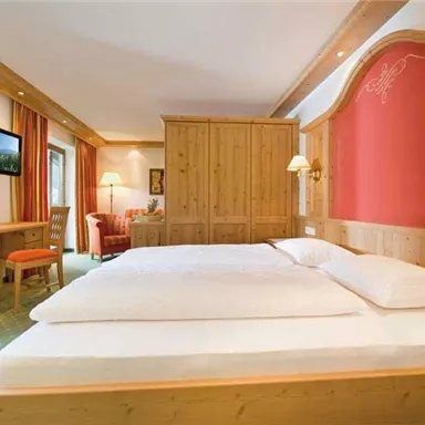 A cozy room with a large bed and wooden furniture. There is a television and a seating area with a red wall and colorful curtains.