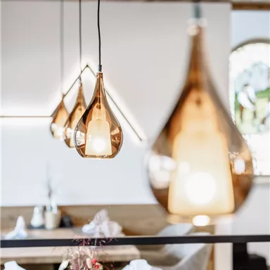 An elegant restaurant with stylish wooden surfaces. Hanging, droplet-shaped lamps create a warm atmosphere.