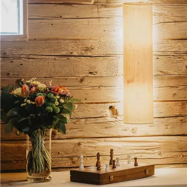 A cozy room with wood paneling. On a table, there is a vase with colorful flowers and a chess game.