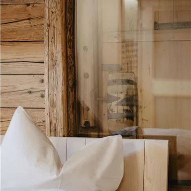 A cozy bedroom with a wooden bed and large pillows. In the background, wooden walls and a window are visible.