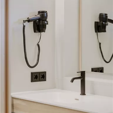 A modern bathroom with a sink and a hairdryer. The room has a bright, simple decor and a mirror.