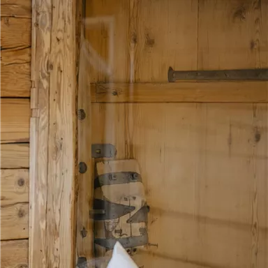 A rustic wooden wall design with a transparent glass door. Simple wooden shelves are visible in the background.