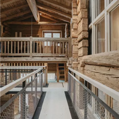 A modern interior with wooden ceilings and large windows. A bridge connects different levels of the space.