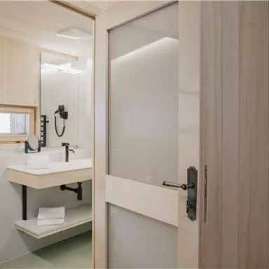 A modern bathroom with bright wooden walls and an elegant shower. There is a sink with a mirror and fresh towels on a shelf.