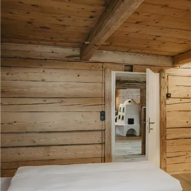 A cozy room with wooden walls and a window. In the background, a door is visible, leading to another room.