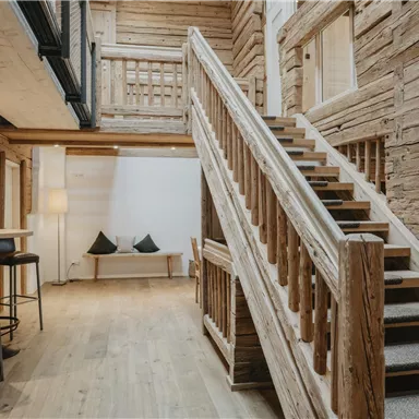 An inviting hallway with wooden walls and a curved staircase. Modern furniture complements the rustic atmosphere.