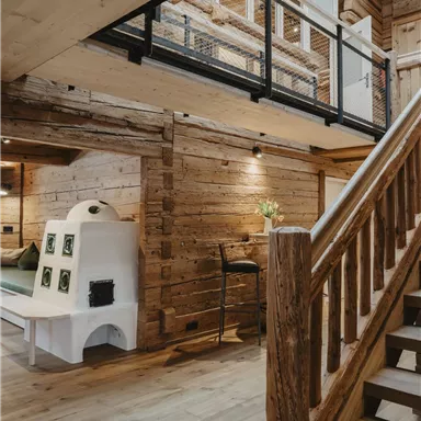 A stylish wooden interior with a staircase and a modern stove. Large windows let plenty of light into the room.