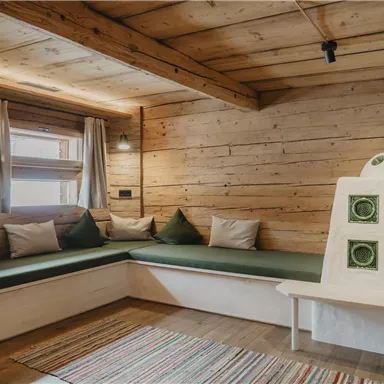 A cozy room with wooden paneling and a seating area with green cushions. A small table and a rug complement the decor.