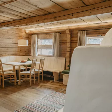 A cozy room made of wood with a dining table and four chairs. Large windows let in a lot of light and create an inviting atmosphere.