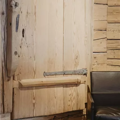 A rustic wooden door with solid fittings and a leather bench next to it. The walls are made of untreated wood, giving the room a natural look.