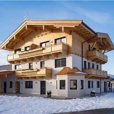 Ein modernes Gebäude im alpinen Stil mit Holzverkleidung und mehreren Balkonen. Die Umgebung ist mit Schnee bedeckt und der Himmel ist klar.