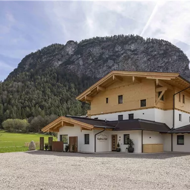 Ein modernes Gebäude mit Holz- und Steinarchitektur befindet sich in einer malerischen Umgebung. Im Hintergrund erhebt sich ein beeindruckender Berg mit grünen Wäldern.