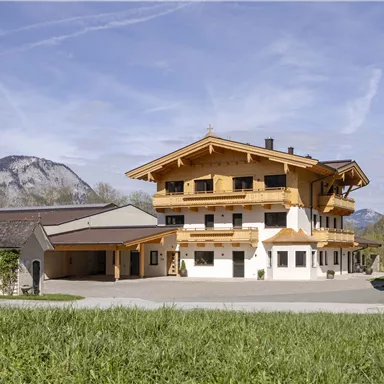 Ein malerisches Gebäude im alpinen Stil, umgeben von grünen Wiesen und Bergen. Der Himmel ist klar und die Landschaft wirkt ruhig und einladend.