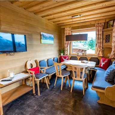 A cozy living space with wood paneling and a seating area. A television hangs on the wall, and a large table invites you to eat.
