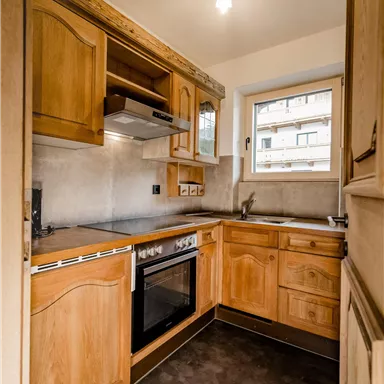 A modern kitchen with wooden cabinets and stainless steel appliances. A window provides natural light and a view outside.