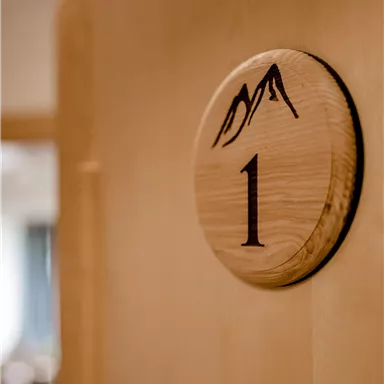 A wooden door sign with the number 1 and a mountain symbol. The background is blurred and shows an indoor area.