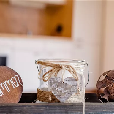A warm welcome greeting with a rustic sign in the shape of an apple. Next to it is a decorative glass and artistic decorative balls.