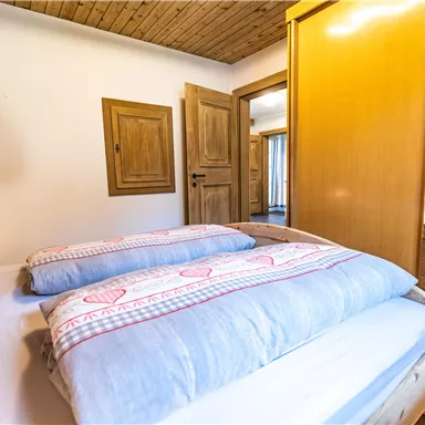 A cozy bedroom with a bed, a wooden ceiling, and a wardrobe. The walls are painted in warm tones, creating an inviting atmosphere.