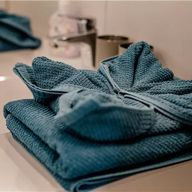 A modern bathroom with stacked blue towels on a sink. The surroundings are bright and clean.