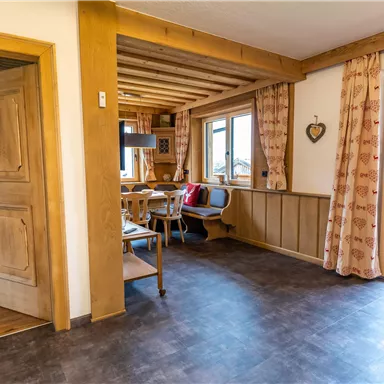 A cozy living space with wooden details and large windows. There is a dining table and access to a balcony.