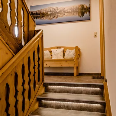 A cozy stair area with a wooden railing and a modern picture on the wall. At the end of the stairs, there is a wooden bench with cushions.