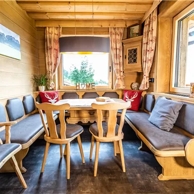A cozy dining area in a wooden cabin. The room is furnished with comfortable benches and a round table, ideal for sociable evenings.