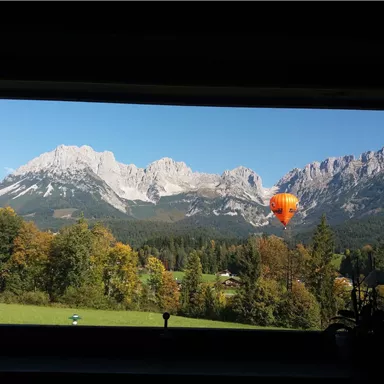 A beautiful mountain landscape with a colorful hot air balloon in the foreground. The sky is clear and the trees are in autumn colors.