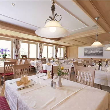 An elegant restaurant with wood decor and festively laid tables. Large windows offer a view of the surroundings and ensure a bright atmosphere.