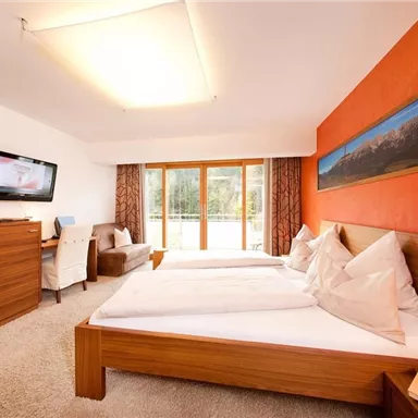 Ein modernes Hotelzimmer mit zwei Betten und einem großen Fenster. Die Wände sind orange und es gibt einen Fernseher sowie Möbel aus Holz.