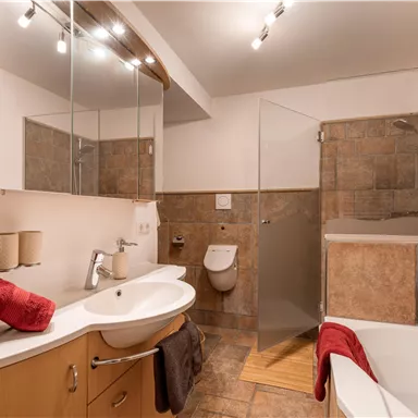 A modern bathroom with a shower and a bathtub. There are wooden and tiled surfaces as well as striking red towels.