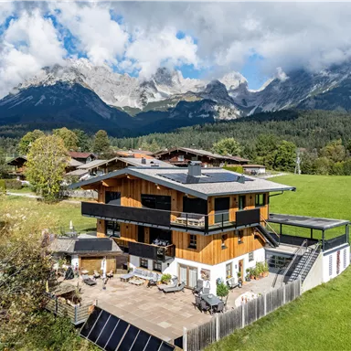 A modern house in the mountains with a spacious outdoor area. The surroundings are green and the mountains are majestically visible in the background.