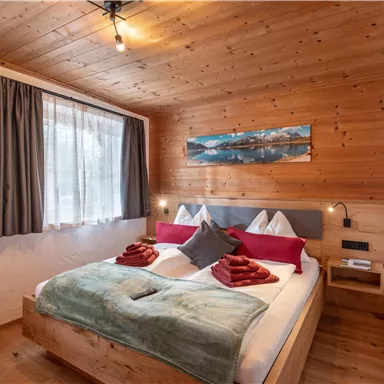 A cozy bedroom with a large bed and wooden walls.  
Soft blankets and cushions in warm colors create an inviting atmosphere.
