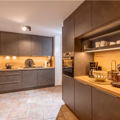 A modern kitchen with dark cabinets and a light wood surface. The lighting creates a cozy atmosphere.