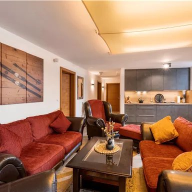 A modern living room with red sofas and an elegant table. The open kitchen is visible in the background and creates a cozy atmosphere.
