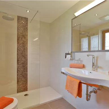 A modern bathroom with a shower and a sink. Orange towels and a bright, friendly atmosphere create an inviting ambiance.