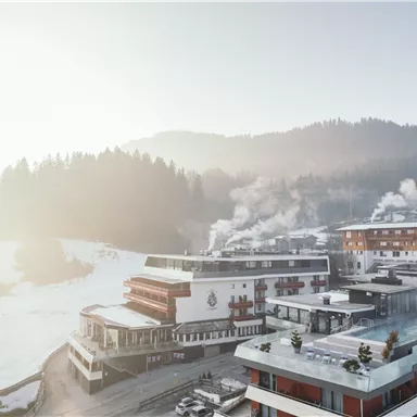A snowy mountain landscape with modern chalets and steaming chimneys. The clear air and gentle hills create a calm and inviting atmosphere.