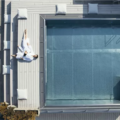 A modern pool with loungers on a terrace. One person is relaxing in a bathrobe next to the water.