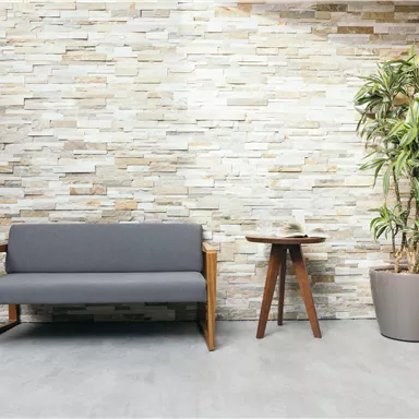 A modern waiting area with a gray couch and a round wooden table. Next to the couch is a large pot with a plant.
