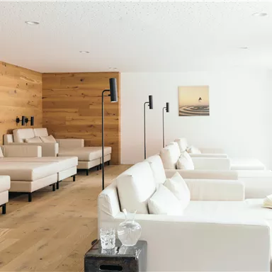 A stylish relaxation room with comfortable, bright loungers and a matching wooden paneling. Large windows provide ample daylight and a serene atmosphere.