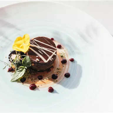An artfully arranged dessert on a blue plate. The chocolate cake is decorated with a flower and berries.