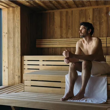 A man is sitting in a wooden sauna and looking out the window. The atmosphere is relaxed and cozy.